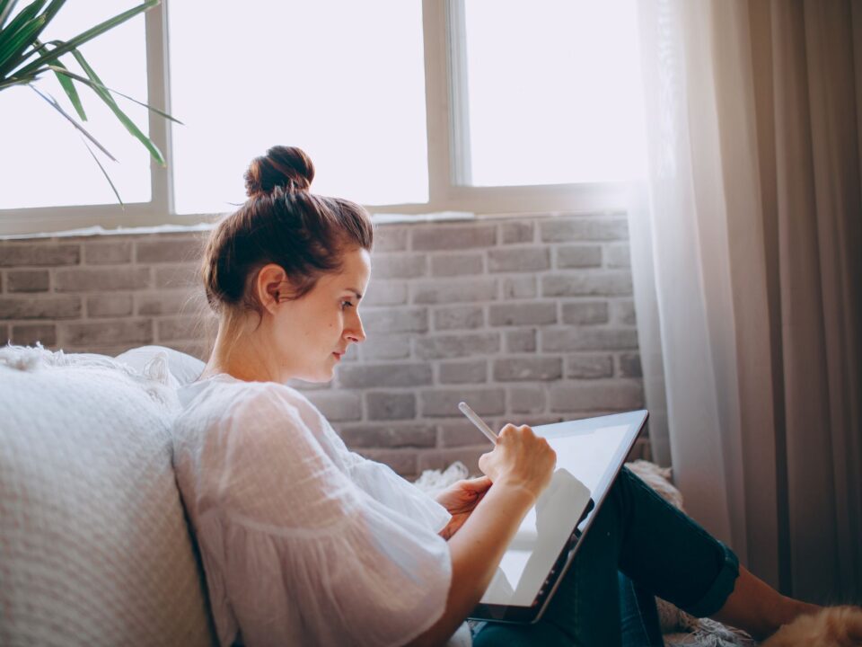 Woman on a sofa by a bright window using a tablet