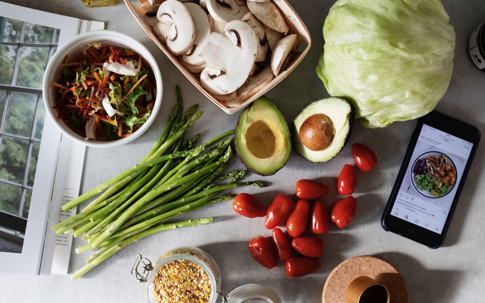 Fresh vegetables, grains and a phone with a meal plan on a kitchen table