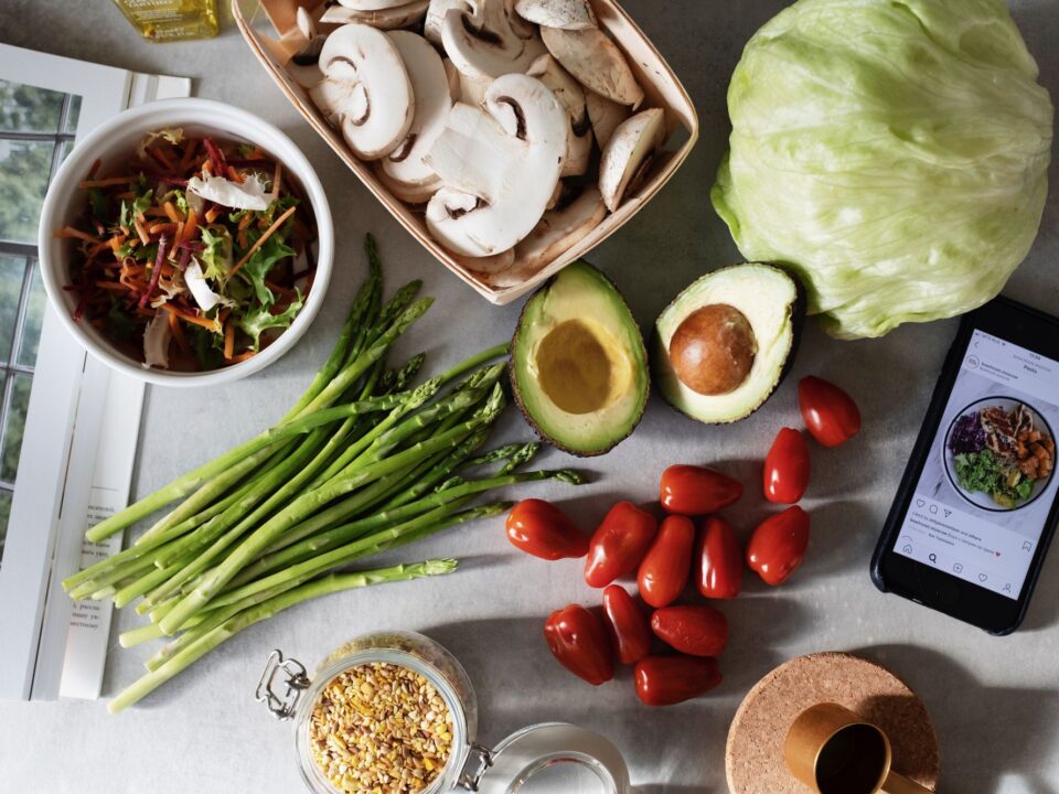 Fresh vegetables, grains and a phone with a meal plan on a kitchen table