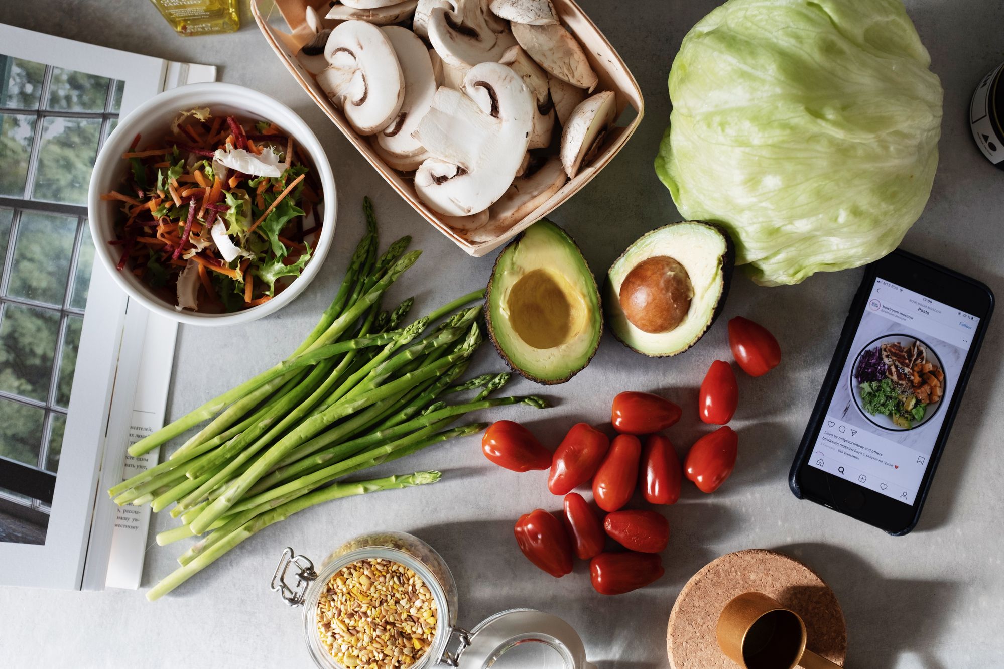 Fresh vegetables, grains and a phone with a meal plan on a kitchen table