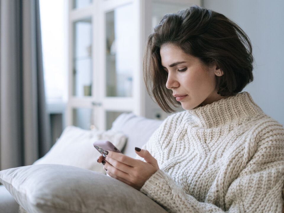 Woman in a knit sweater using her phone on a sofa at home
