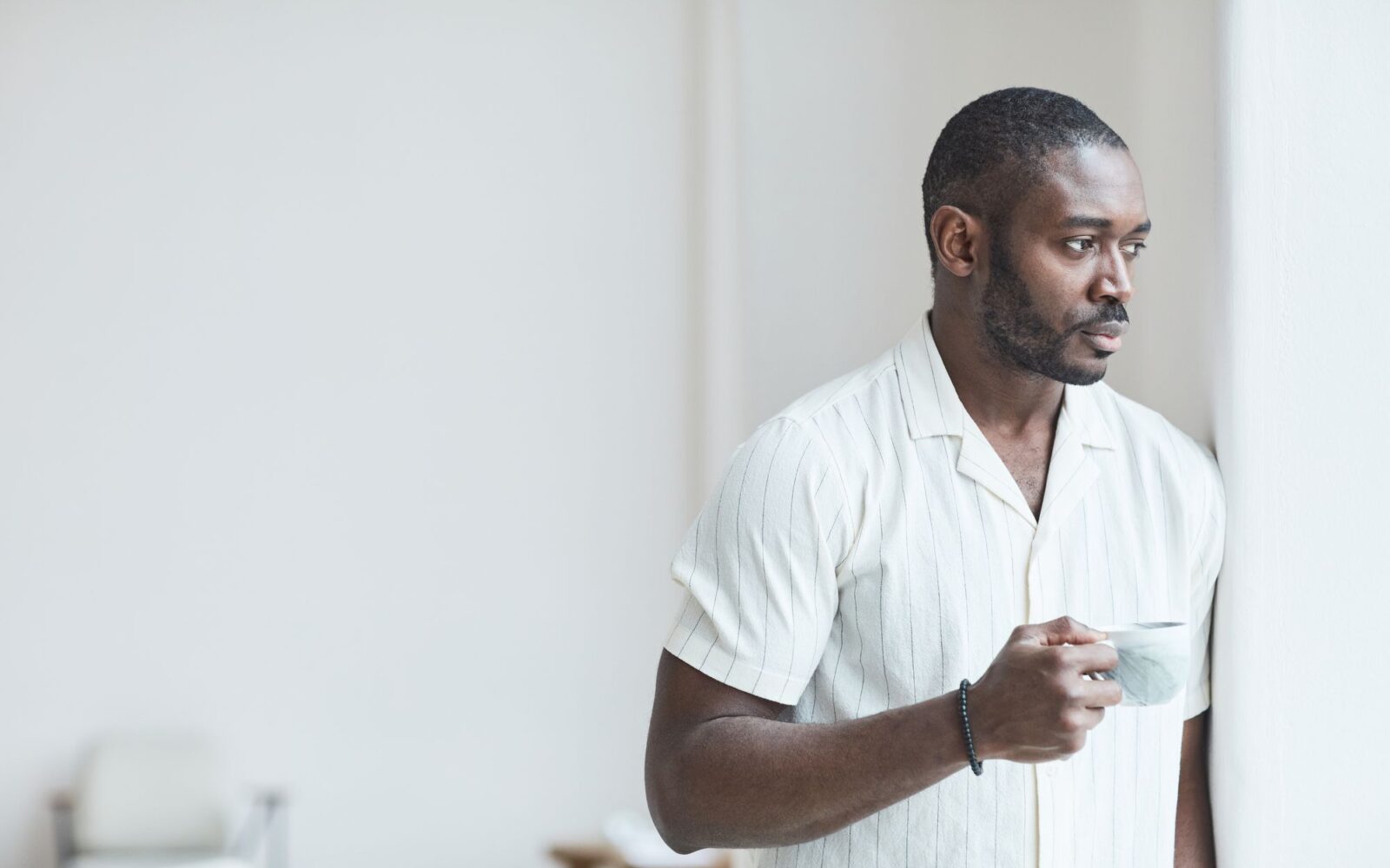 Man holding a cup of coffee and looking out a bright window