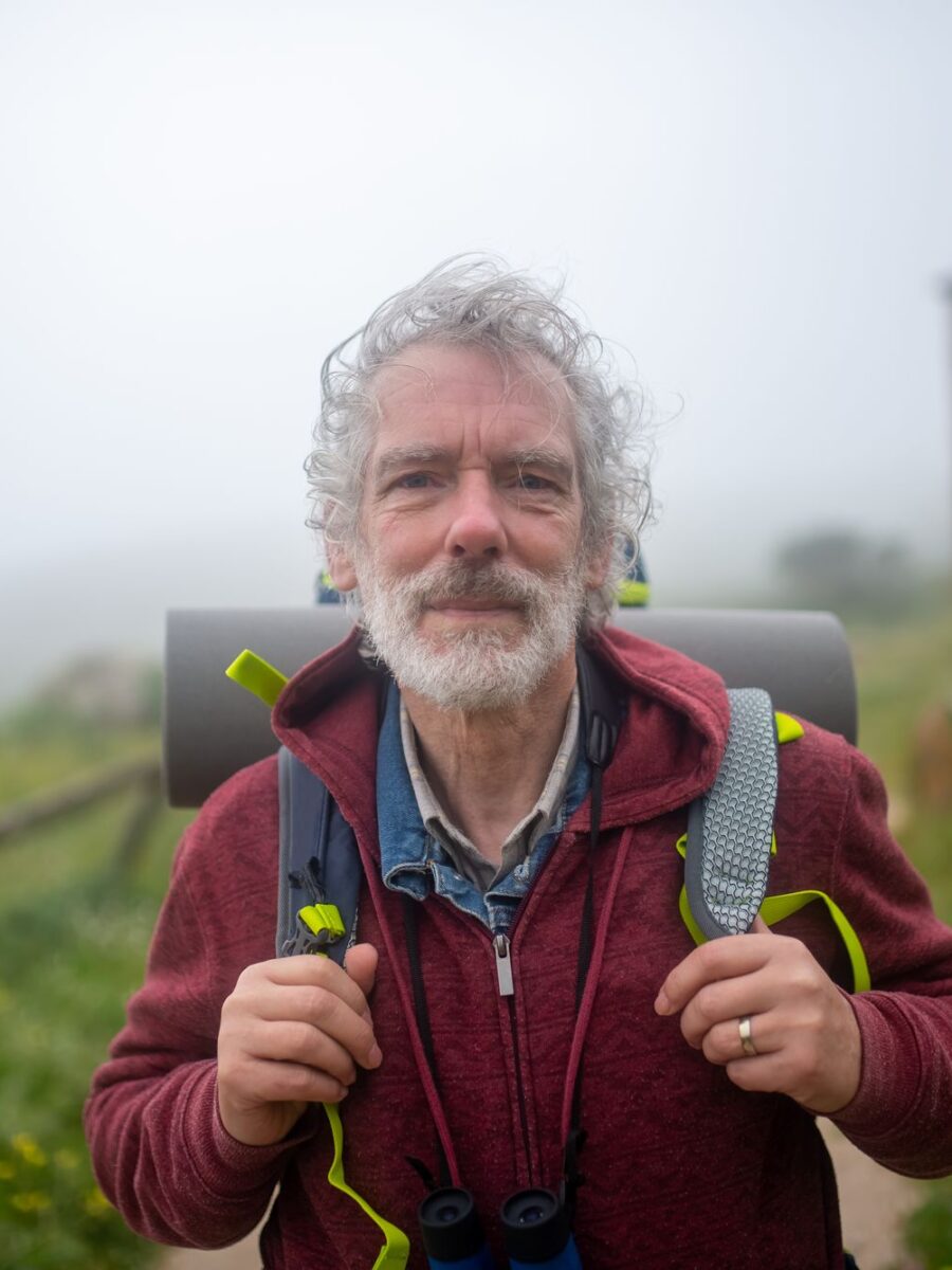 Man in his sixties hiking a misty trail with a backpack