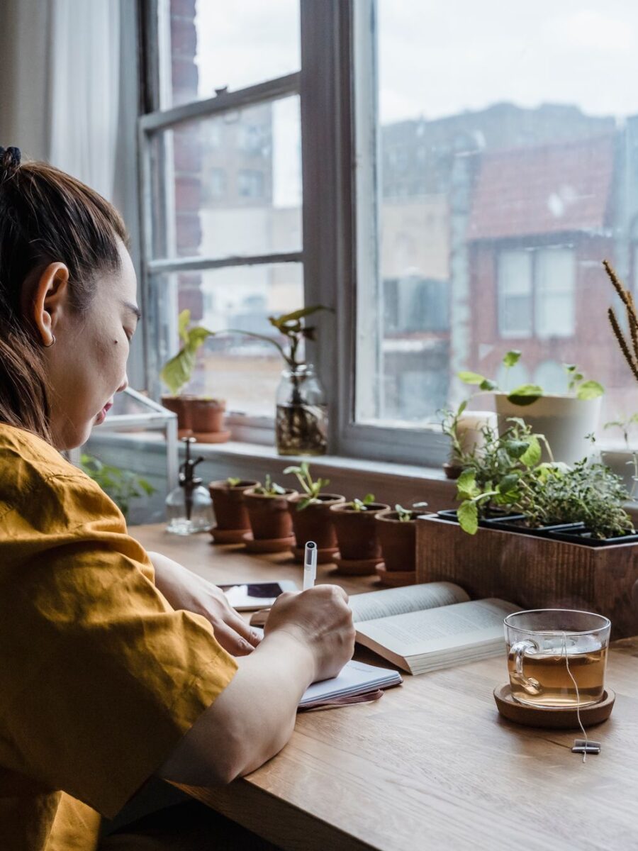 Woman writing in a notebook at a desk by the window